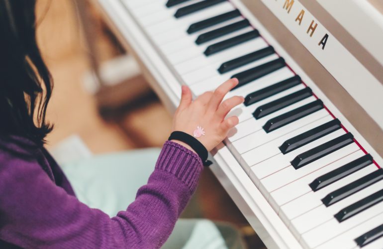 Close up on hand of child playing white piano
